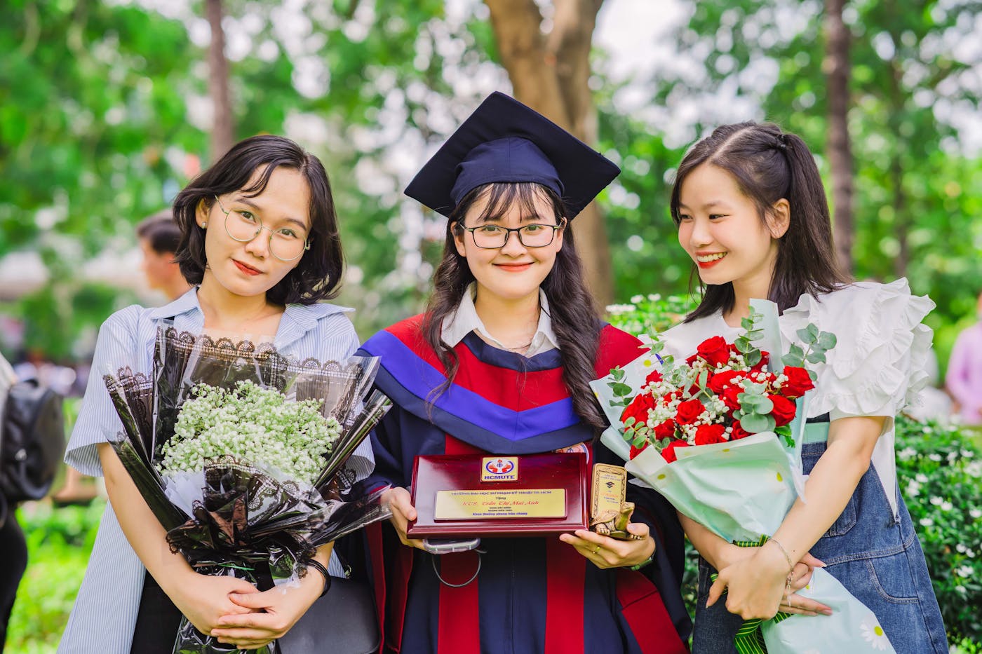 A graduate smiling with friends and flowers after the ceremony